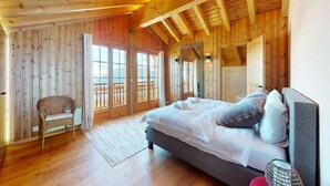 Een slaapkamer in een houten chalet met een bed, een stoel en een balkon.