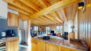Een ruime keuken met houten kastjes, een groot kookeiland, en een eethoek met stoelen en tafels.