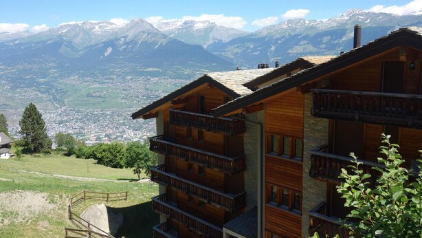 Una xalet de fusta amb diversos balcons que donen a un paisatge de vall i muntanyes.