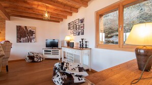 A cozy living room with wooden beams, a television, a white cabinet, and a window with a view of trees. - Chalet in Veysonnaz with hot tub (Veysonnaz)