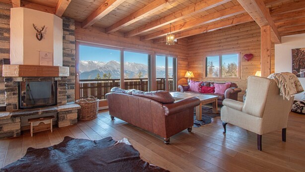 A cozy cabin interior with a stone fireplace, leather sofa, and a view of mountains through large windows. - Chalet in Veysonnaz with hot tub (Veysonnaz)