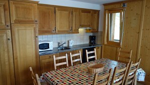 A kitchen with wooden cabinets, a microwave, a coffee maker, and a dining table with chairs. - Spacious apartment with fireplace (Veysonnaz)