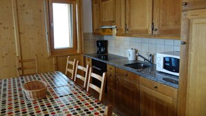 A kitchen with wooden cabinets, a microwave, a coffee maker, a sink, and a table with a polka dot tablecloth. - Spacious apartment with fireplace (Veysonnaz)