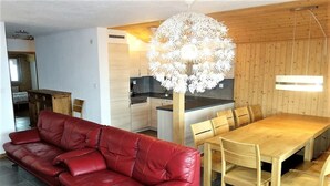 Un salon moderne avec un canapé en cuir rouge, une table à manger en bois et des chaises. Un lustre blanc original est suspendu au-dessus de la table.