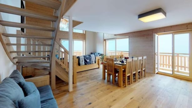 Une pièce spacieuse avec un escalier en bois, un coin repas comprenant une table et des chaises, et de grandes fenêtres offrant une vue dégagée.