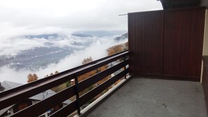 Un balcon donnant sur une vallée et des montagnes, avec une balustrade en bois et un sol en béton.