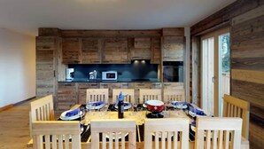 Un coin repas avec un mur en bois, une table dressée pour six personnes et, au fond, un espace cuisine.