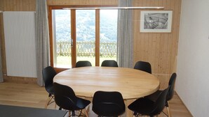 A conference room with a wooden table and black chairs, large windows with a view of a snowy landscape, and a framed picture on the wall. - Apartment in Veysonnaz with Private Balcony (Veysonnaz)