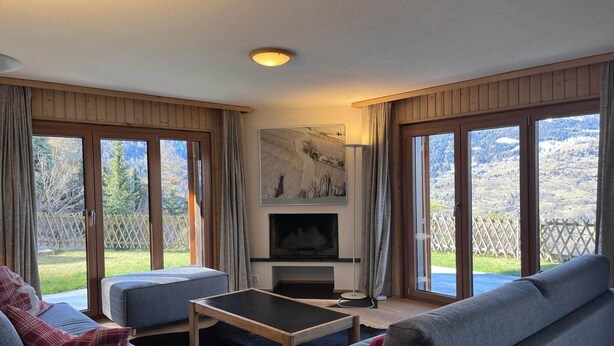 A living room with a fireplace, two sofas, a coffee table, and large windows with a view of a mountainous landscape. - Apartment in Veysonnaz with Private Balcony (Veysonnaz)