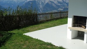 A patio with a stone floor, a wooden fence, and a grill area. - Apartment in Veysonnaz with Private Balcony (Veysonnaz)