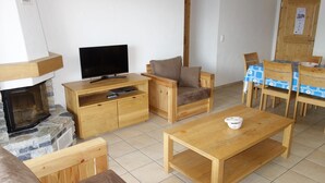 Ein gemütliches Wohnzimmer mit Kamin, Holzmöbeln, einem Fernseher und einem Essbereich mit Tisch und Stühlen.