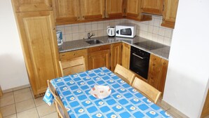 Eine kleine Küche mit Holzausstattung, einer Mikrowelle, einer Kaffeemaschine und einem Tisch mit blauer Tischdecke.
