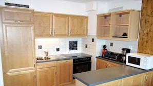 A kitchen with wooden cabinets, a sink, a dishwasher, a microwave, and a coffee maker. - Centrally-located apartment in Veysonnaz (Valais)