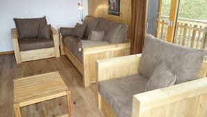 A wooden-floored living room with three sofas and a small wooden table. - Centrally-located apartment in Veysonnaz (Valais)