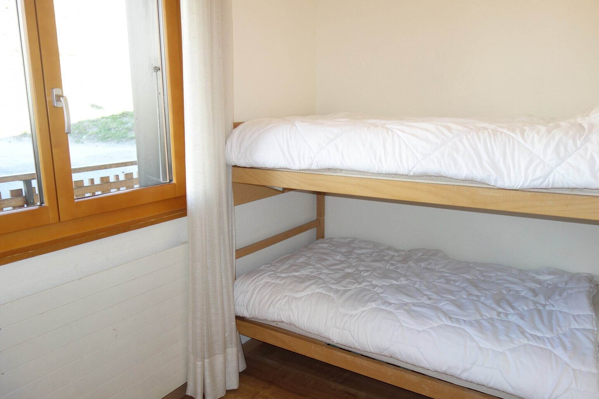 Ein Stockbett mit weißer Bettwäsche in einem Zimmer mit Holzwänden und einem Fenster.