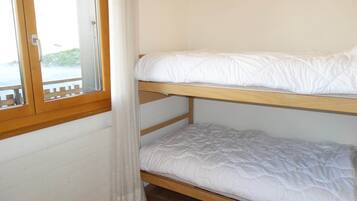 Ein Stockbett mit weißer Bettwäsche in einem Zimmer mit Holzwänden und einem Fenster.