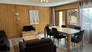 Ein modernes Wohnzimmer mit einer Holzvertäfelung, einem Essbereich mit Holztisch und -stühlen, einem Fernseher und einer Stehlampe.