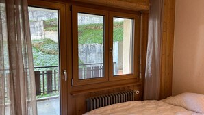 Ein Schlafzimmer mit einem großen Bett, Holzvertäfelung, einem Fenster mit Balkonblick und einer Heizung unter dem Fenster.