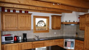 A kitchen with wooden cabinets, a black countertop, a microwave, a coffee maker, and a stove. - Chalet in Veysonnaz with mountain view (Veysonnaz)