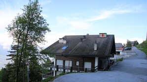 A building with a sloped roof, a small attached structure, and a paved driveway leading to a car. - Apartment in Veysonnaz near Cable Car (Veysonnaz)