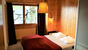 A bedroom with wooden panel walls, a bed with a red blanket, a window with curtains, and a hanging lamp. - Apartment in Veysonnaz near Cable Car (Veysonnaz)