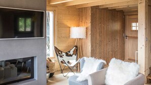 A cozy cabin interior with a fireplace, a large window, a chair with a fur throw, and a lamp. - Chalet in Les Masses with garden (Les Masses)