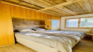 A bedroom with a wooden ceiling, a bed with white bedding, and a window providing natural light. - Apartment in Veysonnaz near Ski Lift (Veysonnaz)