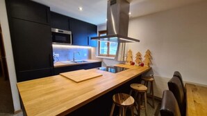 A modern kitchen with a wooden countertop, black cabinets, a stainless steel range hood, and a window with a view. - Apartment in Veysonnaz near Ski Lift (Veysonnaz)