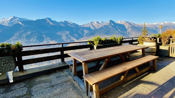 A wooden picnic table with benches, set against a backdrop of snow-capped mountains. - Apartment in Veysonnaz near Ski Lift (Veysonnaz)