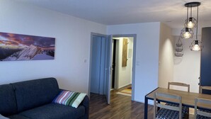 Uma sala de estar moderna com um sofá cinza escuro, uma mesa de jantar de madeira com cadeiras e um quadro de uma paisagem de montanha na parede.