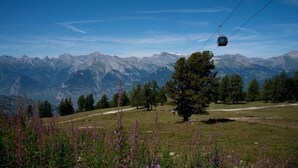 Paisagem montanhosa com um teleférico, árvores e céu claro.