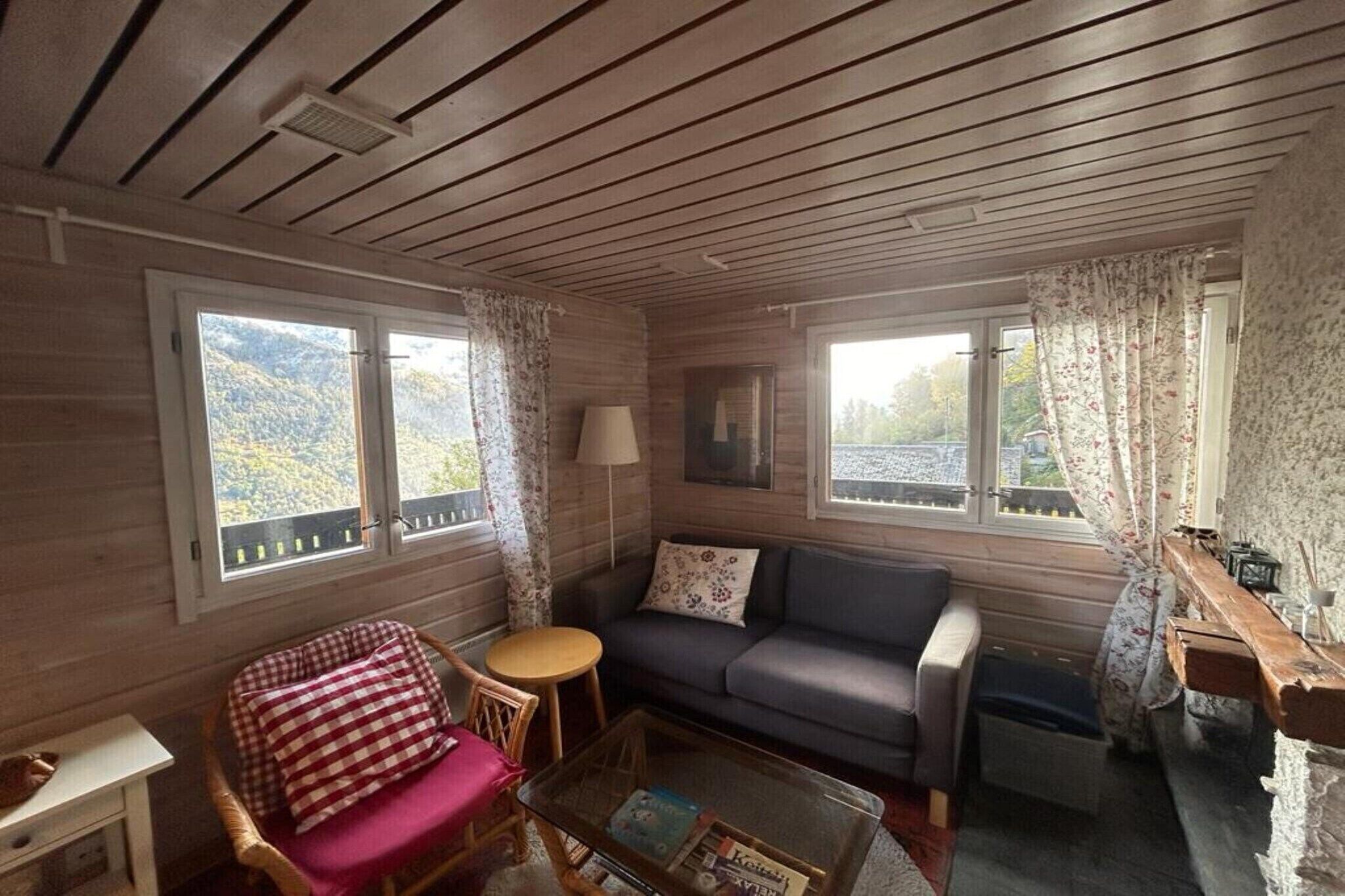 A cozy room with a wooden ceiling, a sofa, a chair, a small table, and a window with a view of trees.