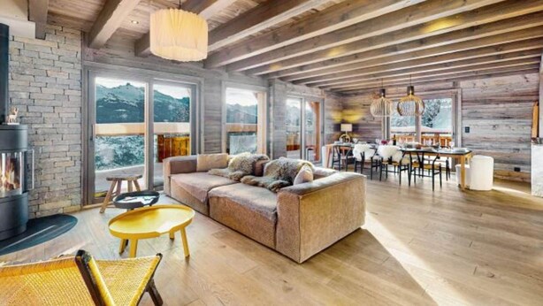 A spacious living area with a wooden ceiling, a fireplace, a sofa, and a dining area with a view of the mountains. - Chalet in Vex near Les Masses Chairlift (Vex)