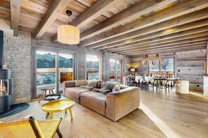 Un vaste espace de vie doté d’un plafond en bois, d’une cheminée, d’un canapé et d’un coin repas offrant une vue sur les montagnes.