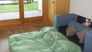 Una habitación con una cama verde, un sofá azul con un peluche, y una puerta de madera que da a un espacio exterior.