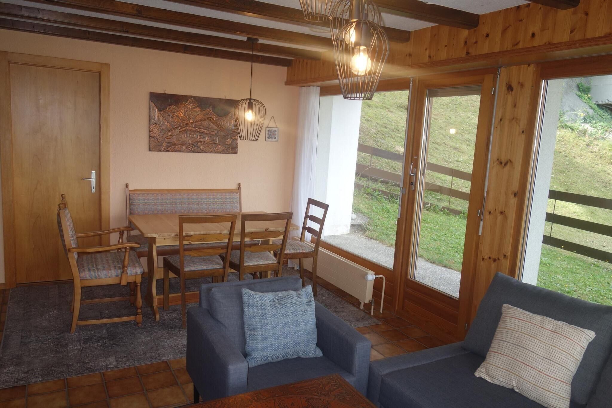 A cozy room with a wooden ceiling, a dining table with chairs, a sofa, and a large window with a view of the outdoors.