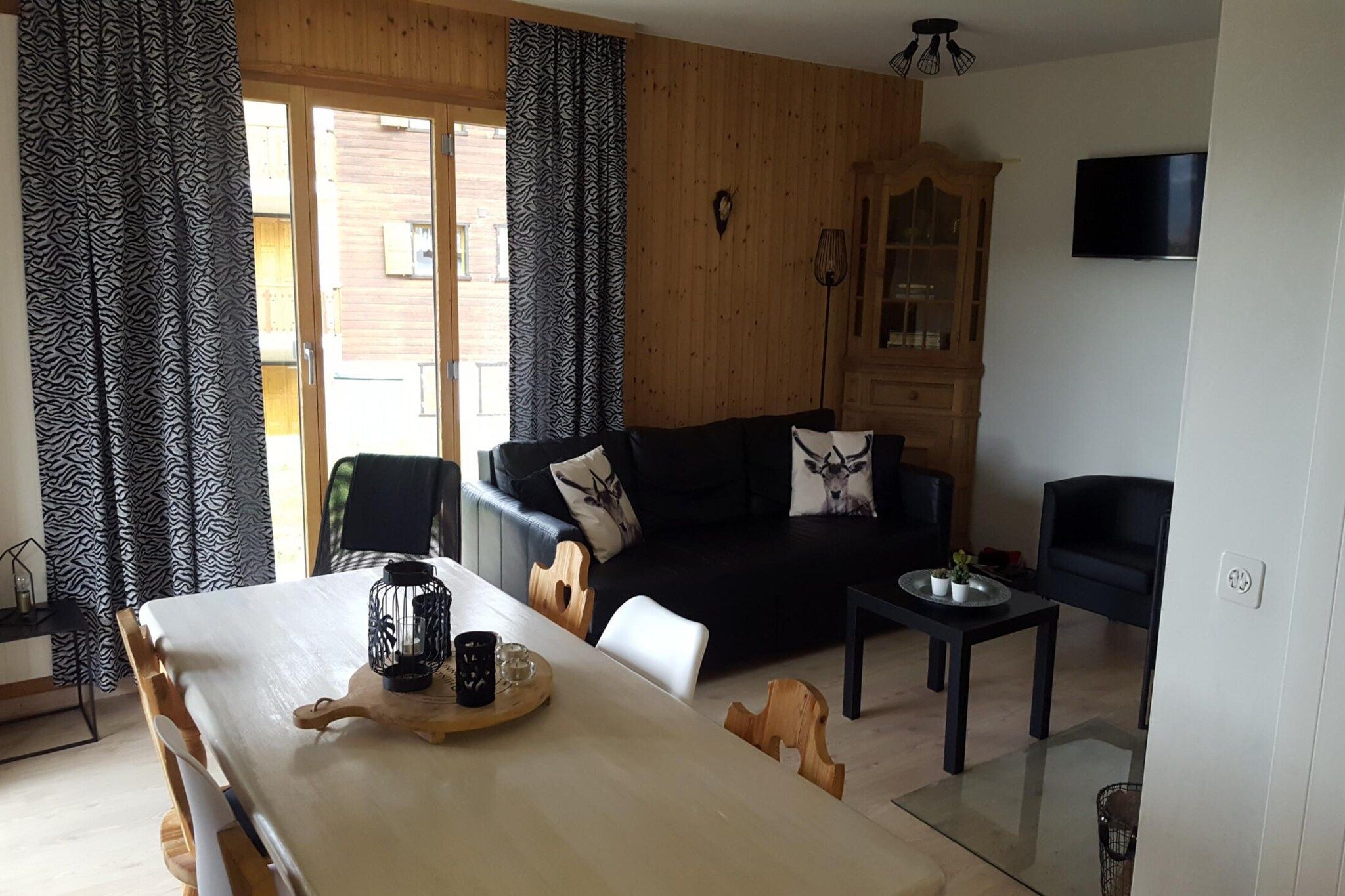 Una sala de estar con sofá, una mesa de comedor con una bandeja y un televisor en la pared.