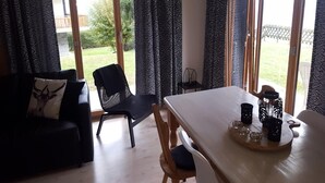 A room with a dining table, chairs, and a view of a garden through large windows.