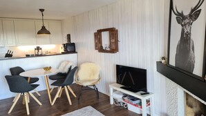 A modern kitchen with white cabinets, a dining area with a round table and chairs, a television on a stand, and a framed deer artwork on the wall. - Flat in Veysonnaz near Ski Lift & Valley Views (Veysonnaz)