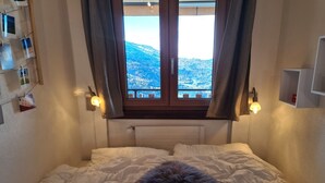 A bedroom with a bed, a window with curtains, a radiator, and wall-mounted lights. - Flat in Veysonnaz near Ski Lift & Valley Views (Veysonnaz)