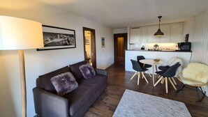 A modern living room with a sofa, a dining table with chairs, a kitchen area with cabinets, and a lamp. - Flat in Veysonnaz near Ski Lift & Valley Views (Veysonnaz)