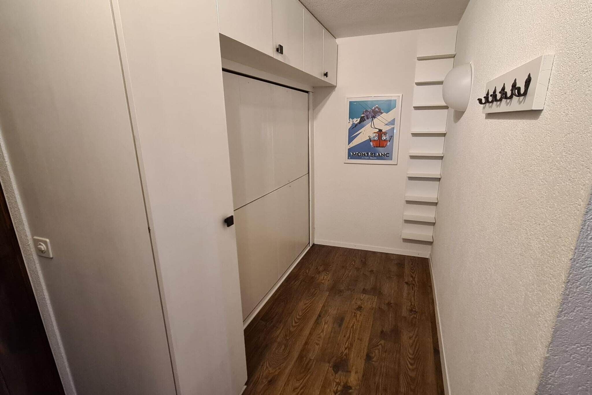 Un corridoio stretto con pavimento in legno, pareti bianche e una porta con sistema scorrevole. Si vede un poster del Monte Bianco sulla parete.
