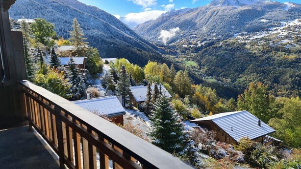 A mountain cabin with a wooden deck, surrounded by snow-covered trees and a valley. - Flat in Veysonnaz near Ski Lift & Valley Views (Veysonnaz)