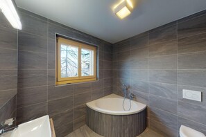 Un baño moderno con una bañera independiente, una ventana y un inodoro.