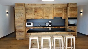A modern kitchen with wooden cabinetry, a black countertop, and three white stools.