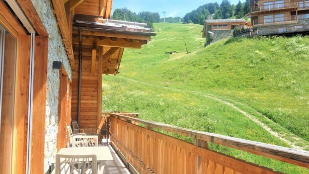 A wooden balcony with a view of a green hillside and a distant building.