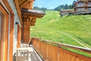 A wooden balcony with a view of a green hillside and a distant building.