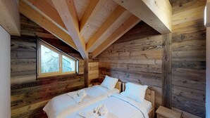 A wooden cabin bedroom with two beds, a window, and a wooden ceiling.