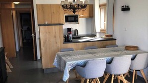 A modern kitchen with wooden cabinets, a central island, and a dining area with a table and chairs. - Apartment in Swiss Alps near Cable Car (Veysonnaz)