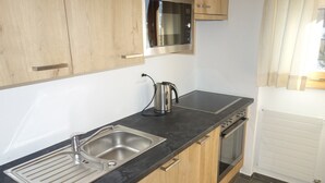 A modern kitchen with a stainless steel sink, a kettle, a microwave, and an oven. - Apartment in Swiss Alps near Cable Car (Veysonnaz)